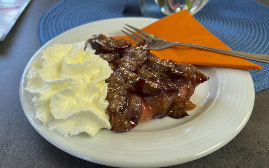 A white plate containing a plum cake with a side of whipped cream. 