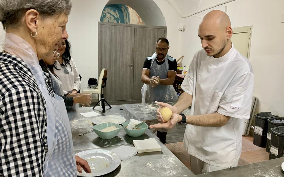 An instructor shows a woman how to shape pasta from a ball of dough