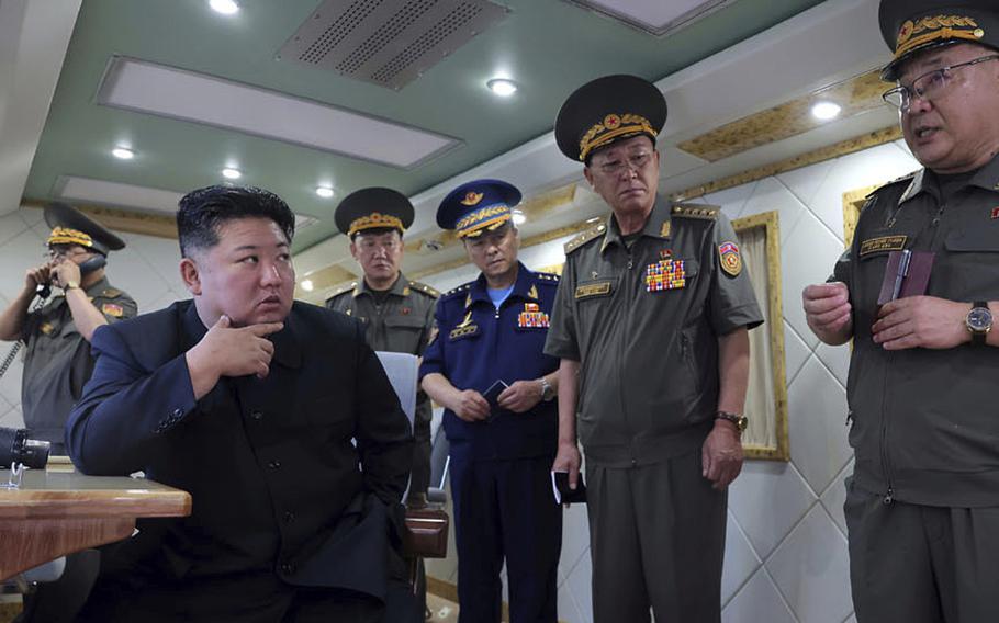 North Korean leader Kim Jong Un sits at a desk while members of the military stand around him.