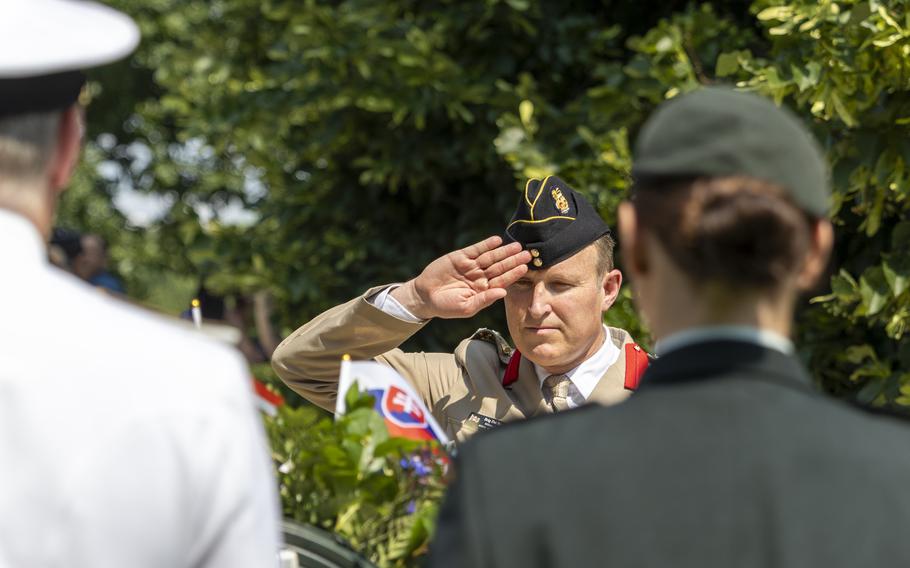 An in-focus man saluting a wreath seen past the slightly out-of-focus shoulders of people in front of him.