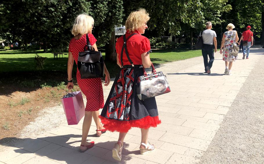 A woman carrying a handbag and wearing a petticoat swing dress with pictures of Elvis Presley walks with another woman through a park in Bad Nauheim, Germany, on Aug. 15, 2021. The spa town hosts a festival in August in honor of Presley, who lived in Bad Nauheim when he was a U.S. Army private from 1958-1960.