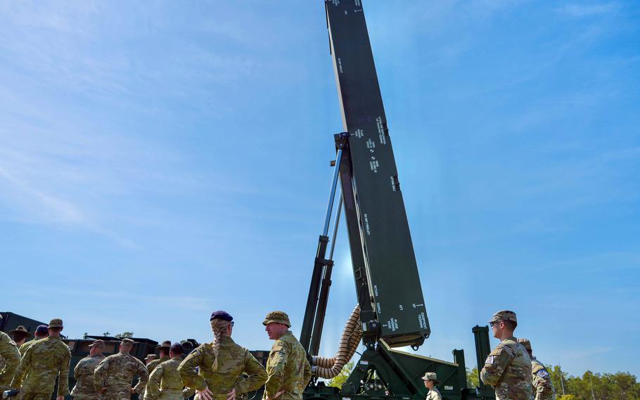 Soliders and allied troops stand in front of the Dark Eagle hypersonic missile system with a blue sky in the background.