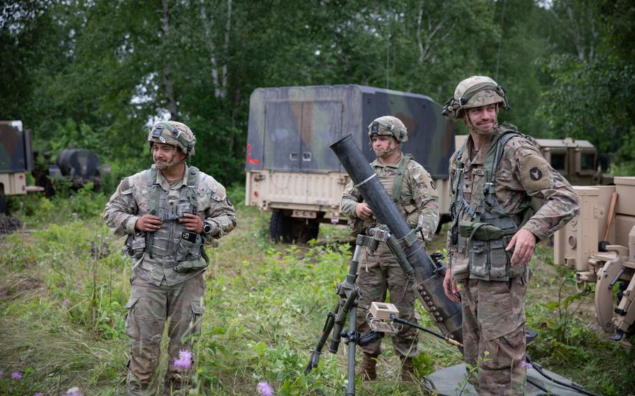 Three Iowa National Guard soldiers standing in a forested area, two of them next to an artillery system.