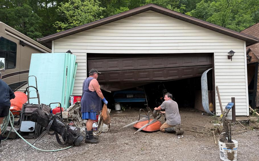 Two people are in front of a garage and other items, like a wheelbarrow.