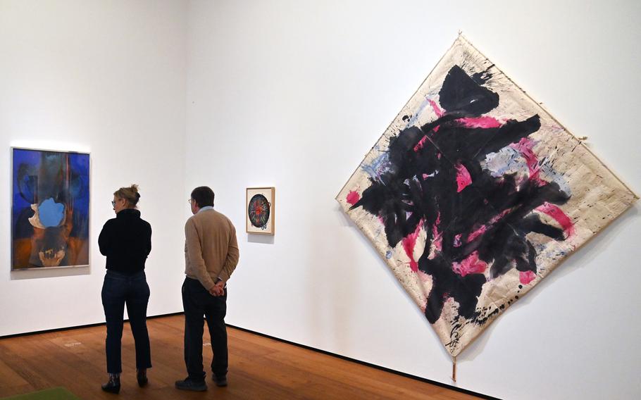 People look at works by various artists hanging on a museum’s walls.