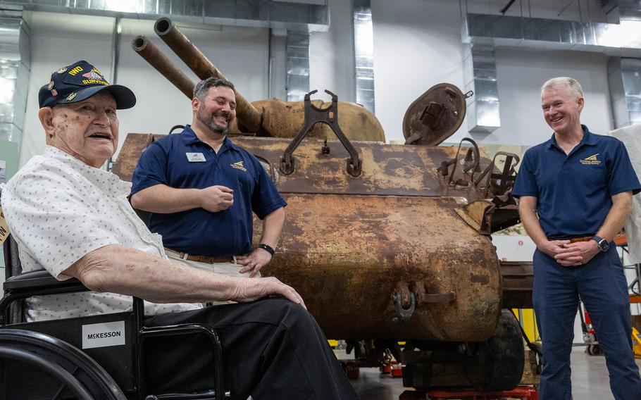 Two men stand in front of a tank with a Marine veteran.