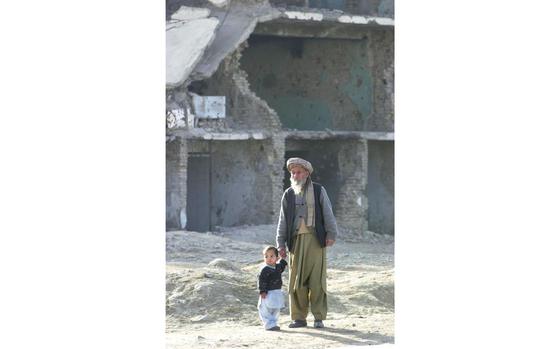 Kabul, Afghanistan, January 4, 2002: An elderly Afghan man guides a young child on the uneven road in front of a bombed out building in Kabul, Afghanistan. The original 2002 caption for the photo read "The very old and the very young have been some of the hardest hit in Afghanistan during more than 20 years of fighting here. U.S. military officials hope to reach out to those in need, by helping aid groups and the Afghan government rebuild the country." Visit the Stars and Stripes store to order a copy of Stars and Stripes' photo book "15 years in Afghanistan," covering the years 2001 - 2016 https://www.stripesstore.com/15yearsinafghanistan-starsandstripesphotobook.aspx META TAGS: Operation Enduring Freedom, War on Terror, Afghanistan, Afghan, 