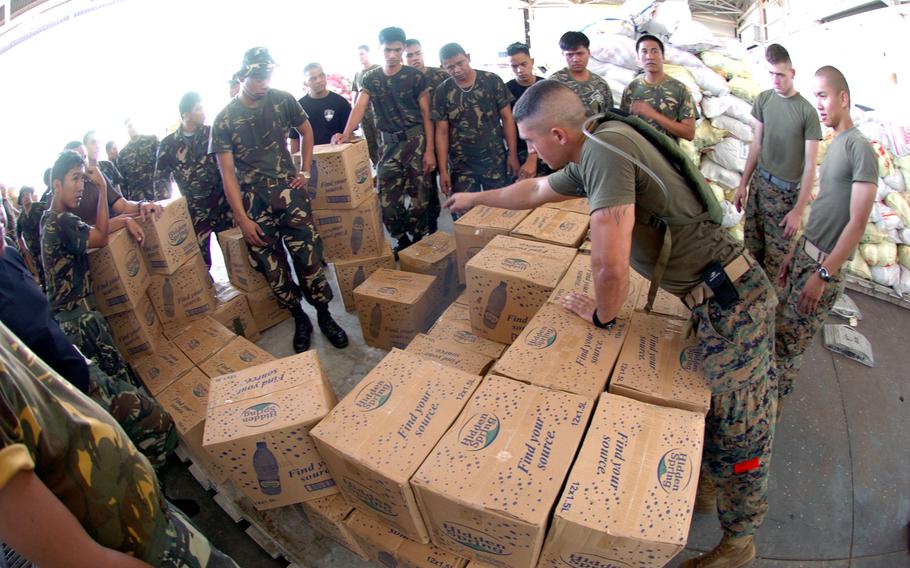 Lance Cpl. Jeffery Pynduss, right, from the 3rd Transportation Support Battalion counts the boxes of water bottles to make sure a pallet isn’t overloaded for helicopters flying relief supplies to families affected from mud slides and flooding in the Philippines.