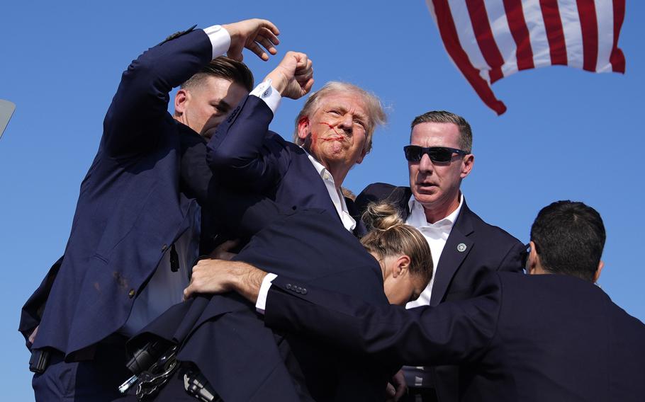 Trump, with blood on his face, raises his fist as Secret Service agents surround him.