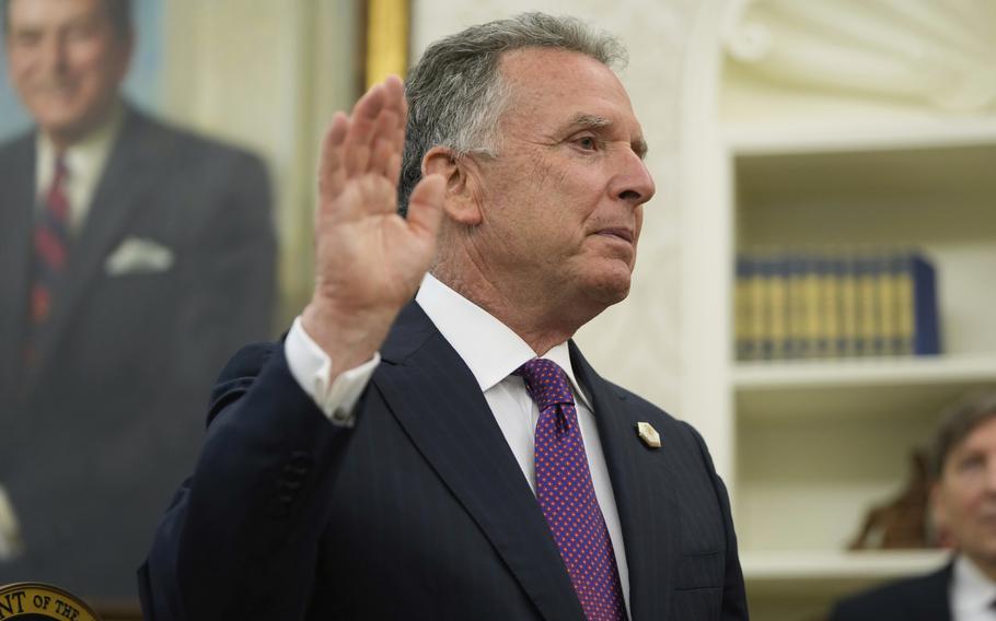 A man in a dark suit holds up his right hand during a swearing-in ceremony at the White House.