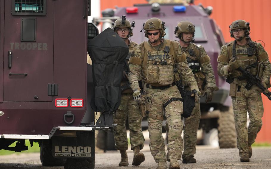 Law enforcement agents walk holding weapons.