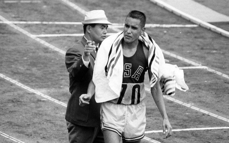 An Olympic official throws a towel over Marine Corps  Lt. Billy Mills after he came in 14th in the marathon at the 1964 Tokyo Olympics. Days earlier, Mills beat 37 of the world's top endurance racers for the gold medal in the 10,000 meters with a record time of 28 minutes, 24.4 seconds.