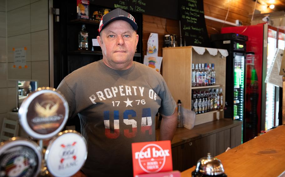 A Polish restaurant owner stands behind the counter of his restaurant wearing a “property of the USA” shirt.