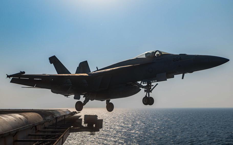 A fighter jet launches off the edge of an aircraft carrier at sea.