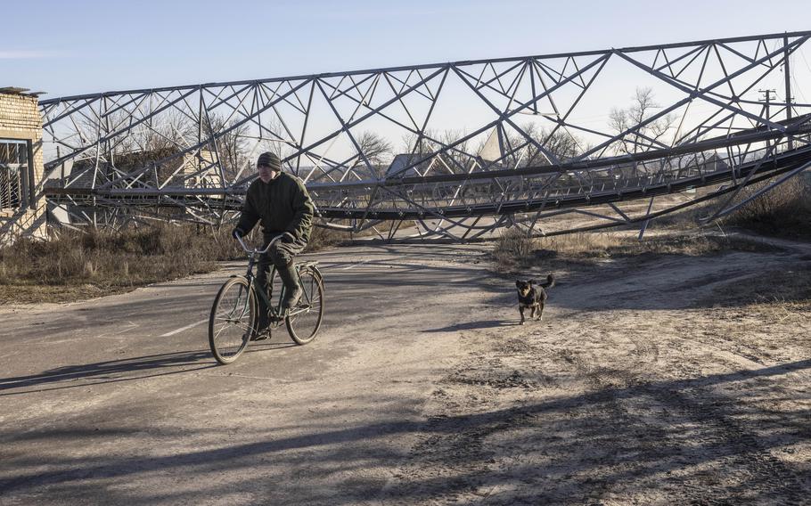 A dog follows a man as he rides past a large electrical tower that fell over onto a road, in the town of Yampil, Ukraine, on Dec. 17.