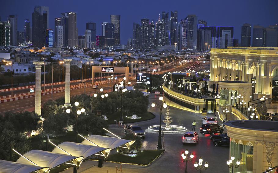 Doha’s skyline at night in the background, with a well-lit complex in the foreground.