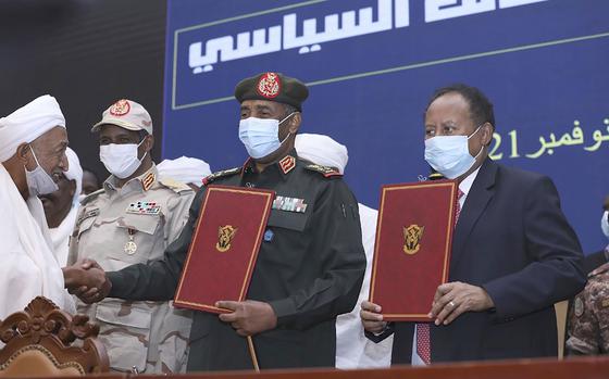 In this photo provided by the Sudan Transitional Sovereign Council, Sudan's top general Abdel Fattah Al-Burhan, center, and Prime Minister Abdalla Hamdok hold documents attended by Gen. Mohammed Hamdan Dagalo, second left, during a ceremony Nov. 21, 2021.