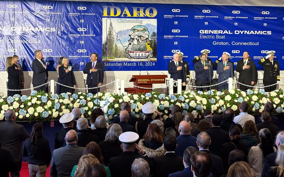 Principal speakers and stakeholders for the pre-commissioning unit (PCU) Idaho (SSN 799) observe the national anthem during a christening ceremony at General Dynamics Electric Boat shipyard facility in Groton, Conn., Saturday, March 16, 2024.