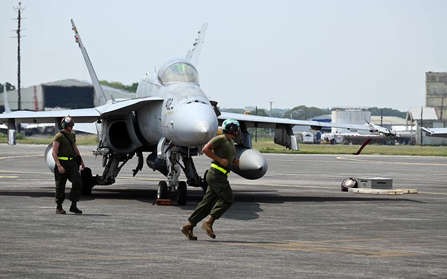 Ground crew members work around a parked F/A-18 fighter jet on the runway, one crew member jogging while another stands by the aircraft.