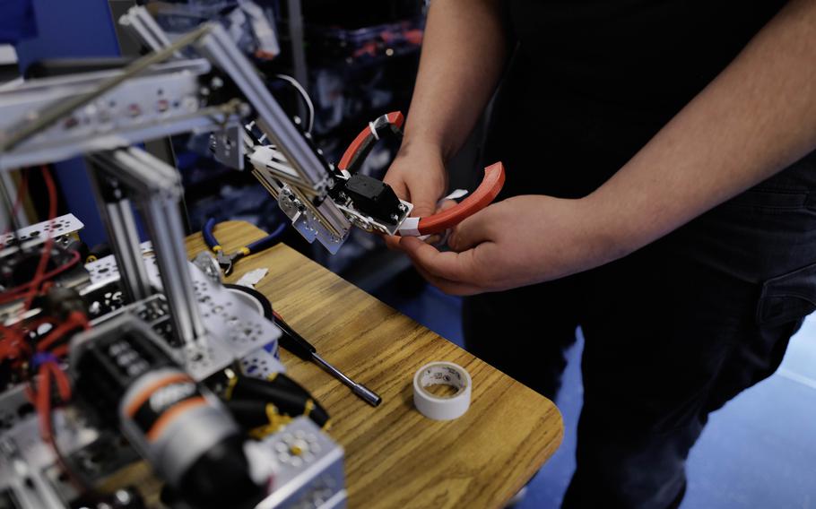 Xander Sanchez, of the Ramstein robotics team, adjust the gripper claw on the team’s robot March 18, 2024. The arm enables the robot to grab small plastic tokens and transport them.