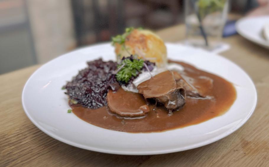 A beef sour roast covered in sauce and served with dumplings and red cabbage.