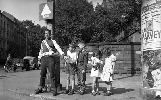 Frankfurt, Germany, Sep. 28, 1949: Charles Brown halts a group of pupils from the Furstenberger Elementary School in Frankfurt until it's safe to cross Furstenberger street. Brown, an eight-grader, is a lieutenant in the Junior Traffic Patrol, a nationwide U.S. safety club dedicated to guarding dangerous street intersections crossed daily by school children. The organization extended its activities to the U.S. Zone of occupation in Germany this schoolyear when forty boys and girls attending the Fursterberger Elementary School took up their special traffic control duties. The children escorted safely to school are, from left to right, Jonathan Lovell, Woody Ervin, Linda Graham and Sally Erikson.

Looking for Stars and Stripes’ historic coverage? Subscribe to Stars and Stripes’ historic newspaper archive! We have digitized our 1948-1999 European and Pacific editions, as well as several of our WWII editions and made them available online through https://starsandstripes.newspaperarchive.com/

META TAGS: Europe; Germany; crossing guard; children; dependents; military family; pupils; students; safety; junior safety patrol; DODDS; DODEA