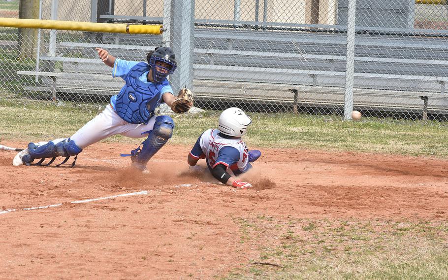 Aviano's Paul Ablang slides safely to score as the ball sails past Sigonella catcher Drake Dawson in a game between the two teams on Saturday, March 18, 2023, at Aviano Air Base, Italy.