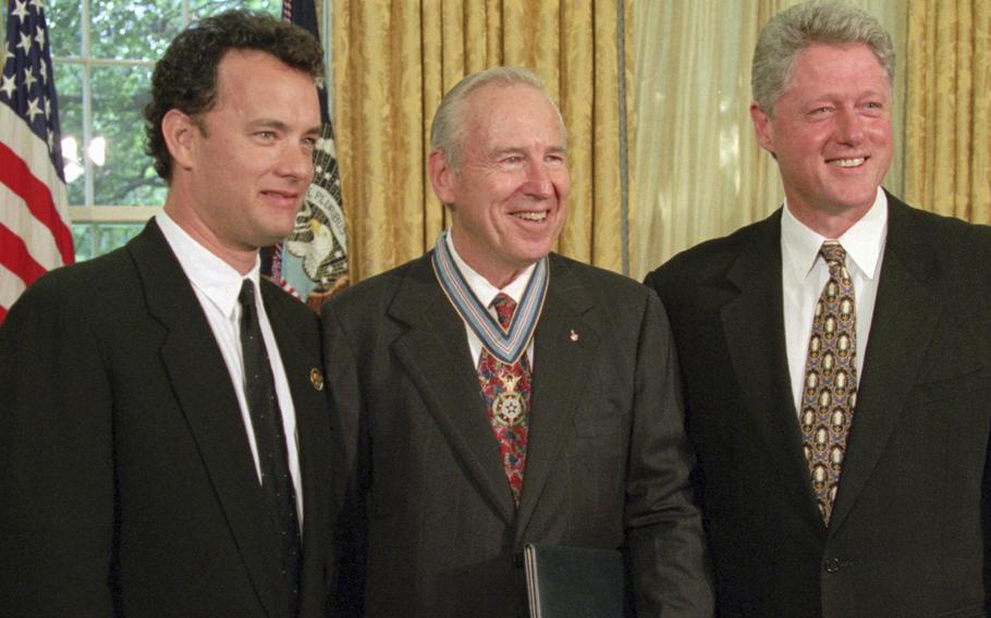 Tom Hanks, Jim Lovell and Bill Clinton, all wearing dark suits, pose for photos in the Oval Office of the White House.