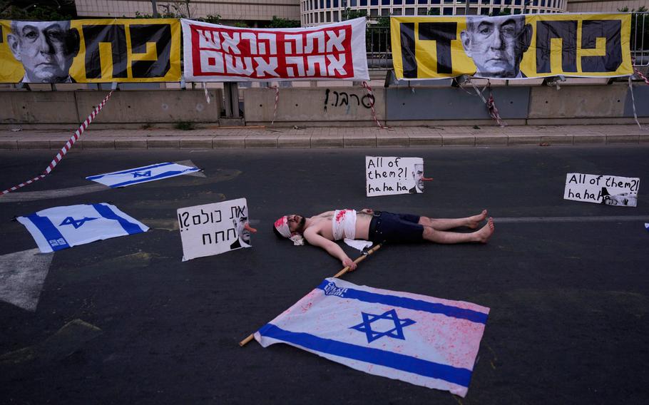 A man laying down on a road with Israeli flags and signs on the road.