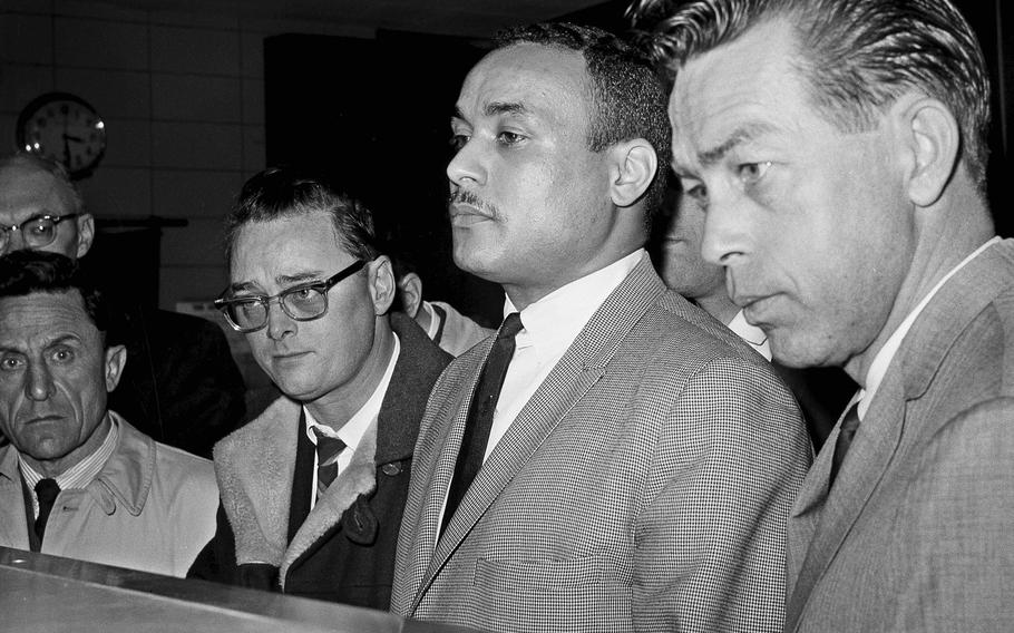 Thomas 15X Johnson, center, is booked as the third suspect in the slaying of Malcolm X, in New York, March 3, 1965. Johnson, one of two men convicted in the assassination of Malcolm X, is set to be cleared after more than half a century, with prosecutors now saying authorities withheld evidence in the civil rights leader’s killing, according to a news report Wednesday, Nov. 17, 2021. Detective John Keeley is at right.