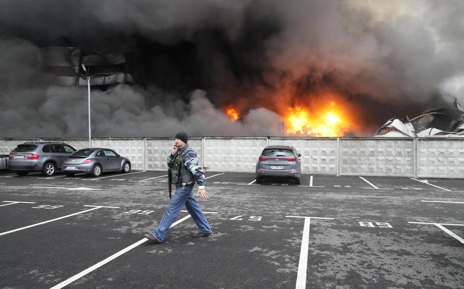 A Ukrainian serviceman walks past as fire and smoke rises over a damaged logistic center after shelling in Kyiv, Ukraine, Thursday, March 3, 2022. Russian forces have escalated their attacks on crowded cities in what Ukraine’s leader called a blatant campaign of terror.