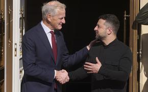 Ukraine President Volodymyr Zelenskyy, wearing a black shirt, and Norway Prime Minister Jonas Gahr Store, wearing a dark suit, shake hands while standing outside a doorway of a government building.