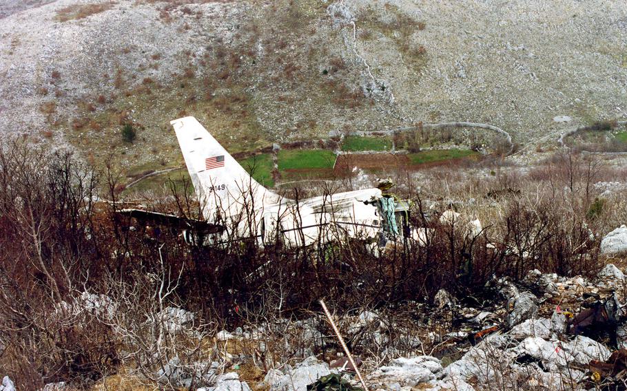 The tailfin and part of the rear fuselage of an airplane rest on the side of a rocky mountain.