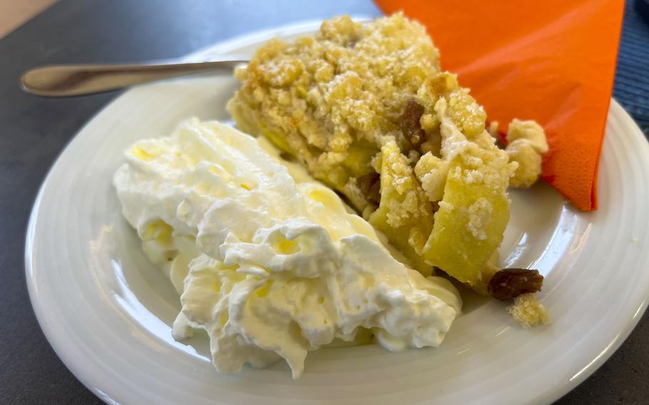 A white plate containing a crumbly apple dessert alongside whipped cream. 