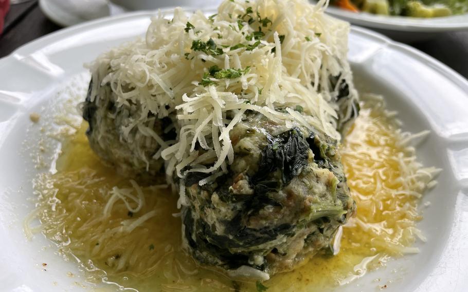 Green spinach-flecked dumplings are topped with grated white cheese and garnished with chopped parsley on a white plate.