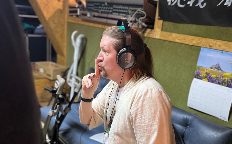 A man wearing headphones gestures with a finger to his lips.