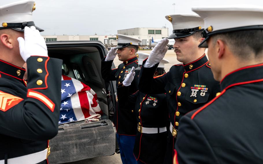 Four Marines salute a casket inside the trunk of a car.