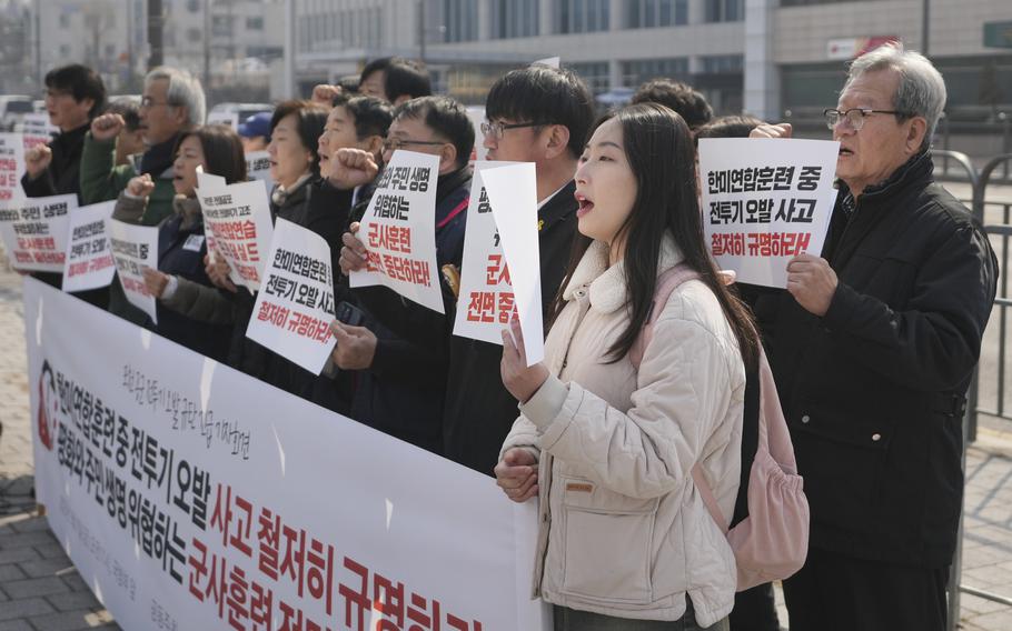 A group of protesters shout slogans and hold up signs including a banner.