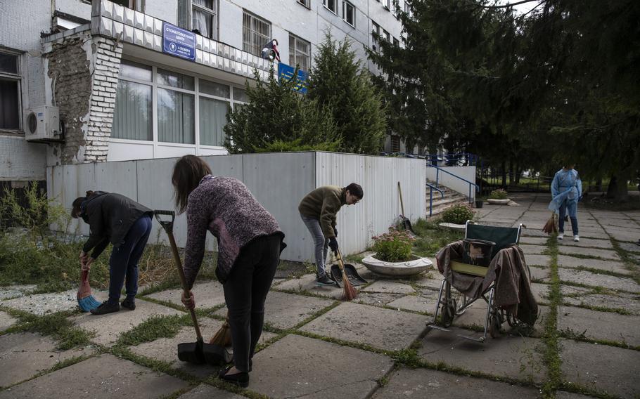 Volunteers and hospital workers clean up broken glass outside a medical diagnostic center next to the Chuhuiv Central District Hospital after it was damaged by a Russian strike on Sept. 10. 