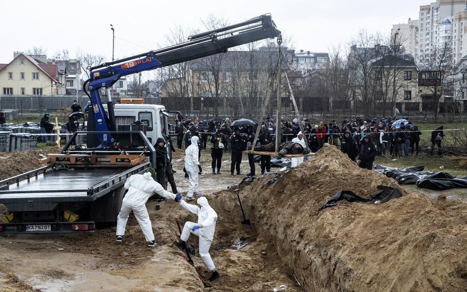 A crowd gathers to watch as workers remove bodies from a mass grave in Bucha on April 8.