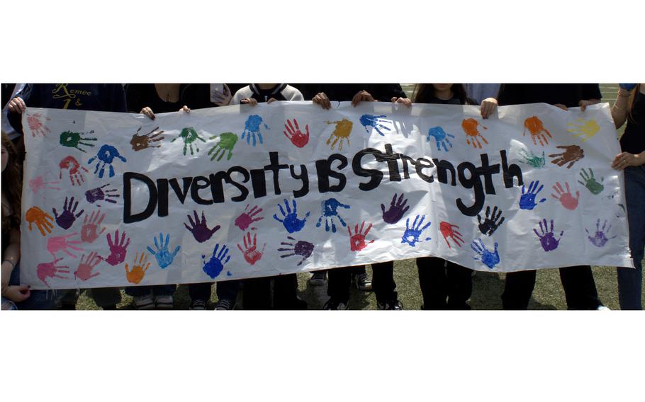 High school students hold a long banner reading “Diversity is Strength” with several colored handprints.