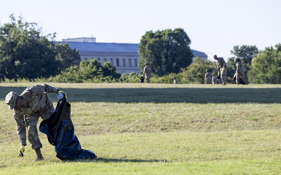 A soldier leans down to pick up trash in the bottom left of the image; farther away in the top right, other soldiers are also collecting trash.