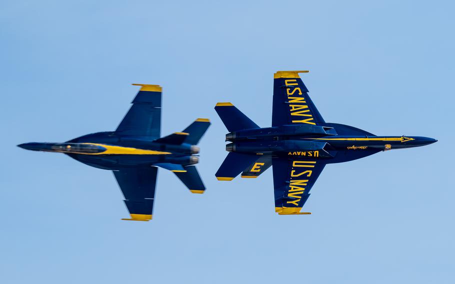 Blue Angels jets pass in close formation headed in opposite directions, with a blue sky above.
