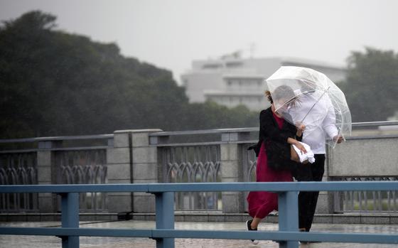 People share an umbrella against strong wind and rain as they walk on a bridge Tuesday, Sept. 20, 2022, in Kawasaki, near Tokyo. A tropical storm slammed southwestern Japan with rainfall and winds Monday, leaving one person dead and another missing, as it swerved north toward Tokyo.