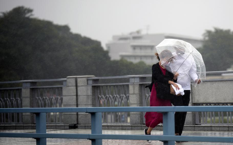 People share an umbrella against strong wind and rain as they walk on a bridge Tuesday, Sept. 20, 2022, in Kawasaki, near Tokyo. A tropical storm slammed southwestern Japan with rainfall and winds Monday, leaving one person dead and another missing, as it swerved north toward Tokyo.