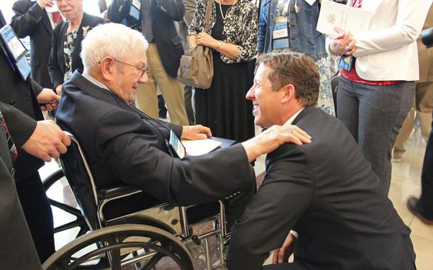 McPherson in a wheelchair talks with Adams, who is kneeling in front of him.