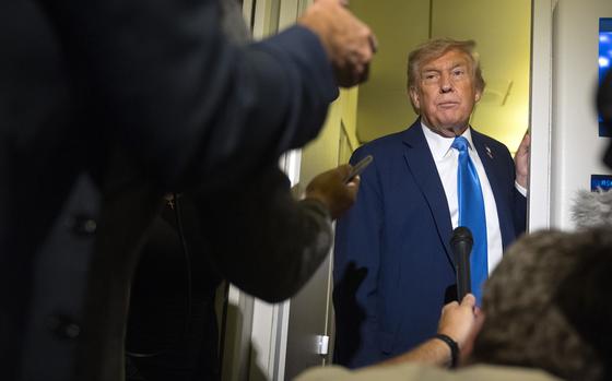 President Donald Trump seen in a door frame, with reporters’ microphones and recorders in front of him.