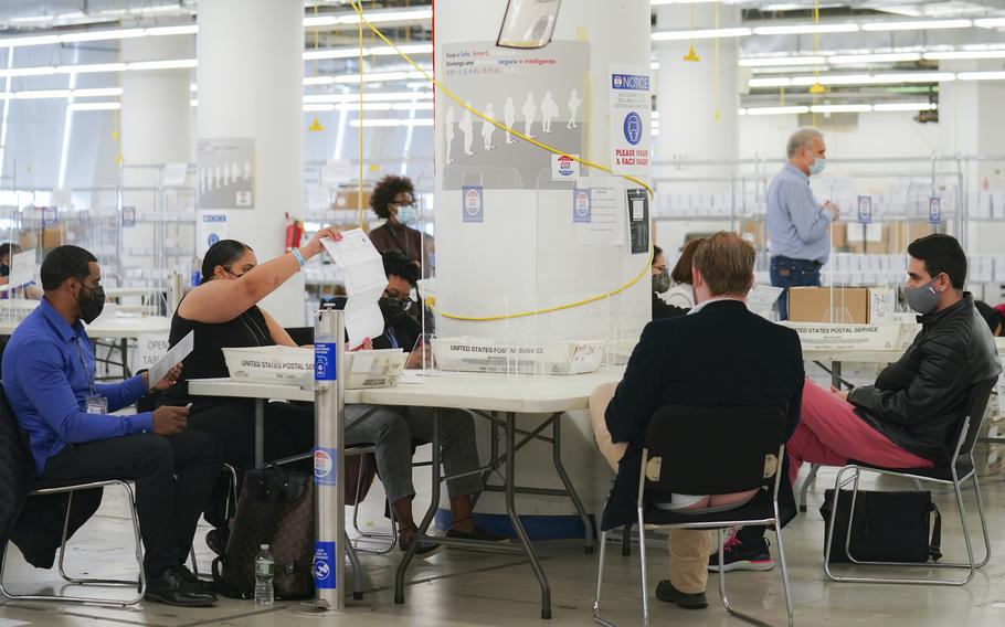 Polling workers inspect and count absentee ballots as poll watchers sit opposite, Nov. 10, 2020, in New York. 