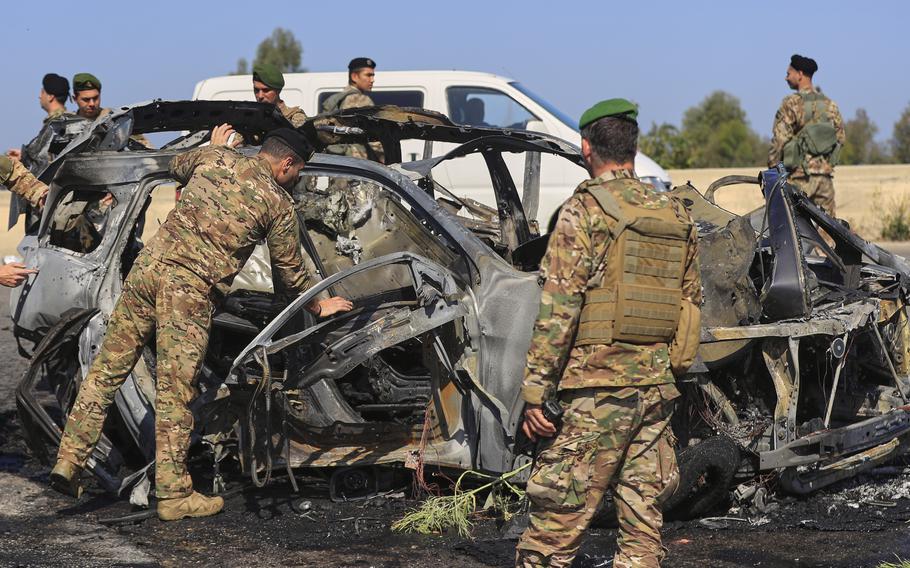 Soldiers gather around a charred vehicle.