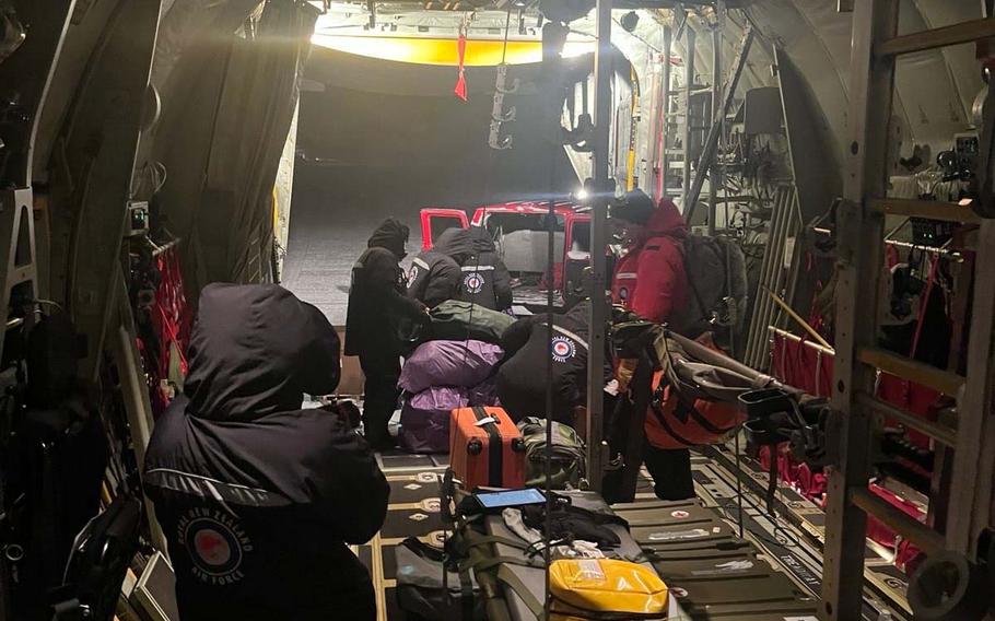 Medical personnel in dark uniforms attend to a patient on a stretcher inside the cargo bay of a military transport aircraft. 